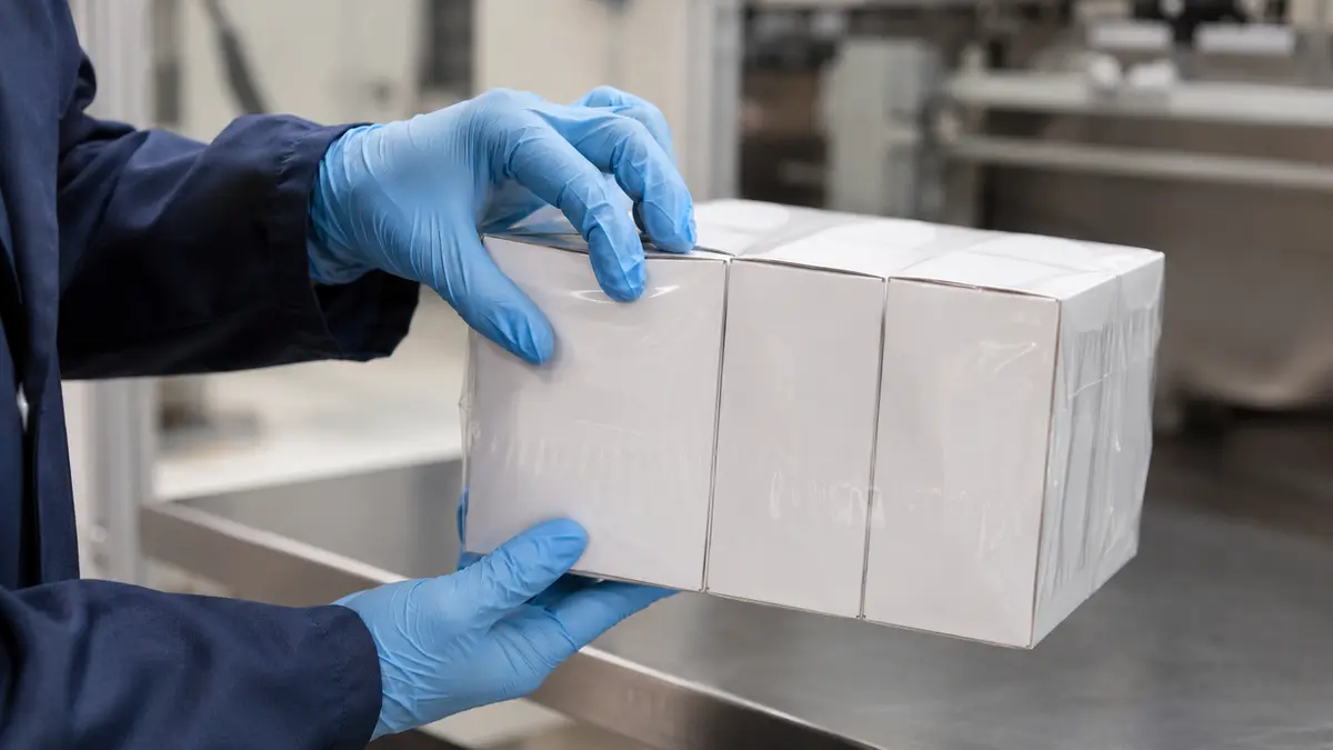Technician inspecting lightweight paperboard cartons after shrink wrapping for signs of distortion